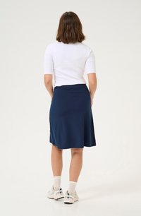 Marineblaue knieumspielende Rock aus weichem, dehnbarem Material, kombiniert mit einem weißen, taillierten Oberteil. Das Model trägt weiße Sneakers und Socken in Crew-Länge.