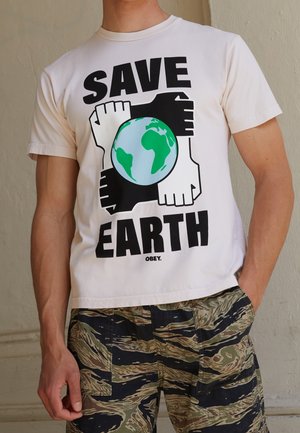 Persona con una camiseta blanca que tiene el texto "SALVAR LA TIERRA", manos en blanco y negro formando un cuadrado alrededor de una ilustración de la Tierra en verde y azul.
