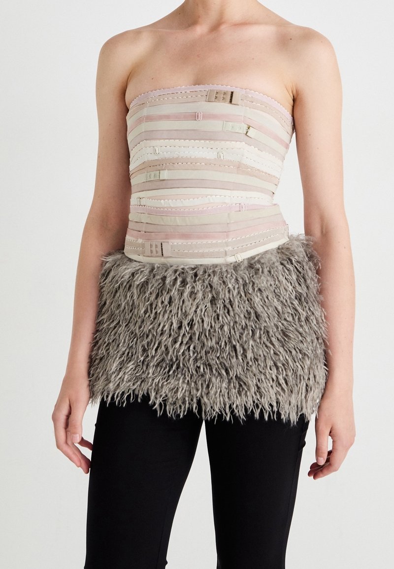 Top bez ramínek s texturovanou béžovou a růžovou tkaninou, která má vodorovné pruhy a zapínání, zdobený chlupatým šedým kožíškem na spodním lemu.