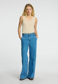 Beige strikket tanktop og højhvide lyseblå flared jeans. Outfittet har et tekstureret strikdesign og en klassisk denimfinish.