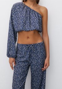 Blaues Blumen-Crop-Top mit asymmetrischem Design und einem langen Ärmel. Kombiniert mit passenden Blumen-Hosen, beide aus leichtem Stoff.