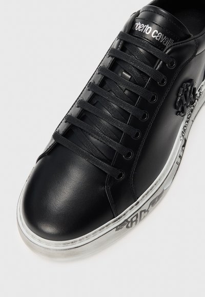 Black leather sneaker with black laces, branded "roberto cavalli" on tongue, ornate black emblem on side, and white sole with black graphic print.