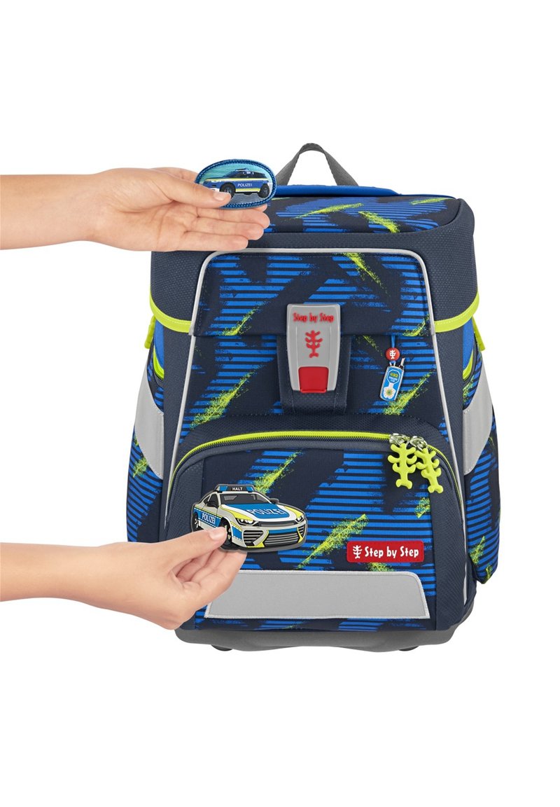 Sac à dos bleu et noir avec des accents verts. Présente un patch de voiture de police, une fermeture à glissière grise et une étiquette de logo, mettant en valeur un design texturé.