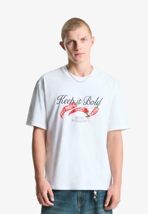 Hvid bomulds T-shirt med trykt tekst og grafik i sort og rød, med korte ærmer og en afslappet pasform.