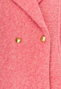 Flauschiger rosa Mantel mit einer strukturierten Oberfläche, der ein doppelt geknöpftes Design aufweist und mit zwei großen goldenen Knöpfen als Akzenten versehen ist.