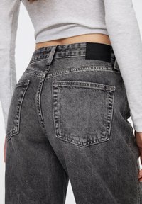 Jean en denim gris taille haute avec un effet délavé, comprenant deux poches arrière, des coutures visibles et une étiquette noire sur la ceinture.