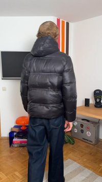 Must must puffer-jakk mustriga kapuutsiga, millel on tikandmuster ja läikiv pind. Kantsitud tumesiniste teksade kohal heledas siseruumis.