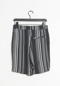 Costumi da bagno a righe bianche e nere con elastico in vita e una piccola tasca laterale. Realizzati in tessuto leggero, appesi a un gancio nero.