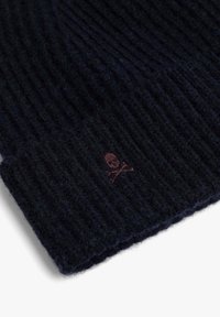 Gorro de punto en azul marino oscuro, con textura acanalada. Pequeño logo marrón de calavera y huesos cruzados cosido en el borde. Material suave de mezcla de lana.
