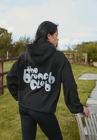 Felpa nera realizzata in tessuto morbido con una grande grafica bianca e giocosa che dice "il club del brunch" sul retro. Presenta una tasca frontale e cappuccio.
