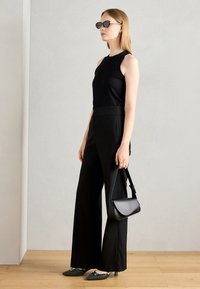 Top negro sin mangas combinado con pantalones anchos de talle alto negros. Accesorios incluyen gafas de sol negras y un pequeño bolso negro. Zapatos verdes texturizados.