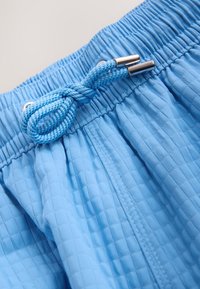 Short en tissu bleu texturé avec une taille élastique et un cordon bleu noué avec des embouts métalliques.