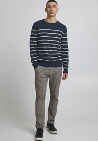 Mørkeblåstripet genser med hvite striper, rund hals, ribbestrikkede mansjetter, kombinert med lysegrå bukser og mørke joggesko. Enkelt design.