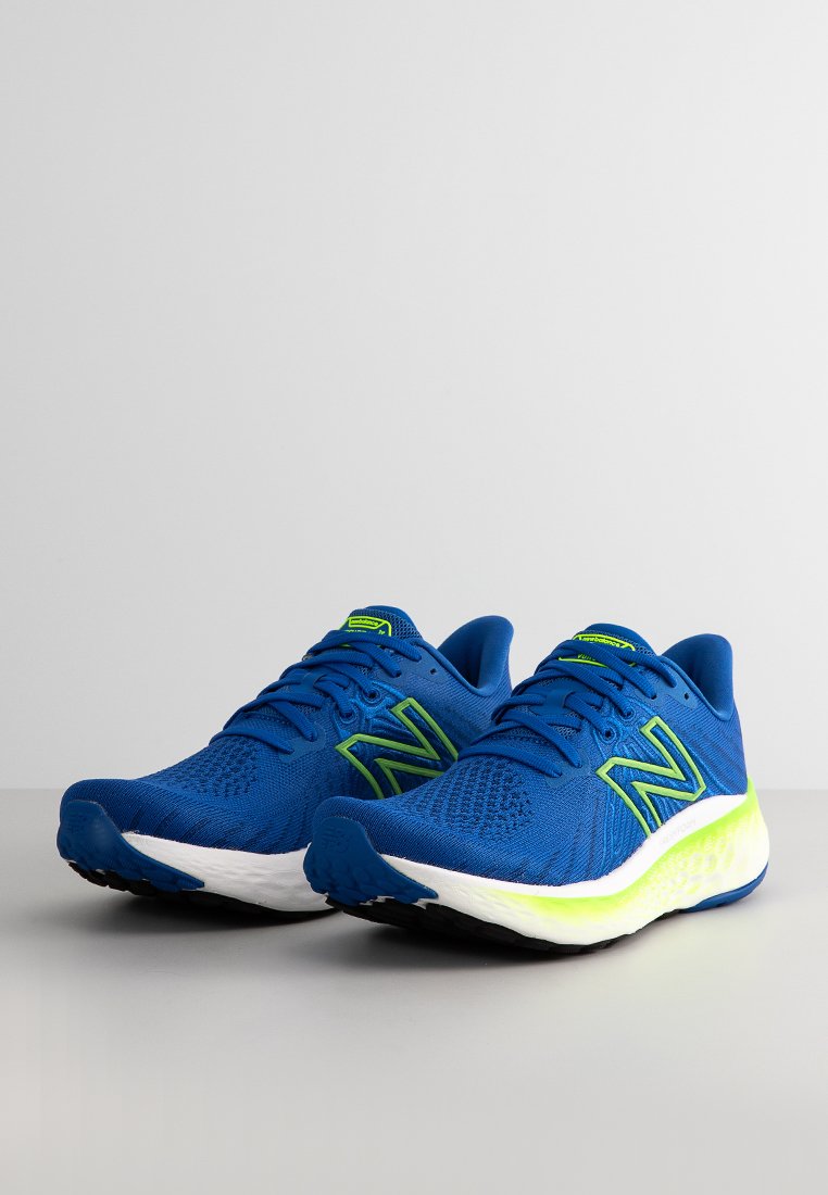 Zapatillas deportivas azules hechas de malla con una superficie texturizada, que presentan un logo verde y detalles en verde, una suela acolchada con un degradado en blanco y amarillo.