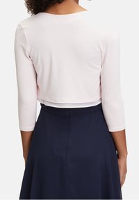 Camiseta corta de color rosa claro con mangas de tres cuartos, combinada con una falda azul marino. La parte superior presenta una textura simple y suave, y un escote redondeado.