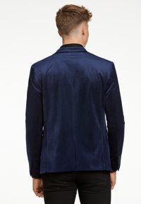 Marinblå sammetblazer med en elegant design, två sidofickor och knäppta ärmslut. Slät textur med en subtil lyster.