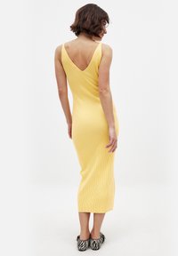 Robe en maille côtelée jaune avec un dos en V profond, silhouette ajustée et bretelles réglables. Associée à des chaussures à motifs noir et blanc.