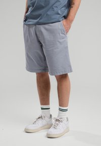 Gray cotton shorts with side pockets and a straight cut, paired with white sneakers and green-striped ankle socks. Simple and casual design.