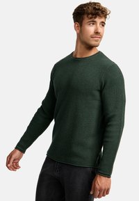 Pull en tricot gaufré vert avec manches longues et col ras du cou. Tissu texturé, fentes sur les côtés et détails côtelés aux poignets et à l'ourlet.