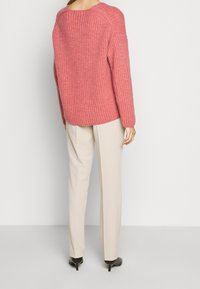 Maglione rosa a costine con una vestibilità rilassata, scollatura rotonda e spalle cadenti, abbinato a pantaloni crema e tacchi neri.
