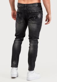 Úzké černé džíny s odřeným detailem, pěti kapsami a koženou nášivkou na zadním pase, kombinované s bílými teniskami.