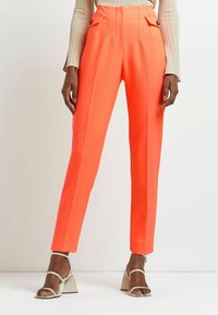 Klart orange byxor med hög midja, två framfickor, skarpa veck och en slät tygstruktur. Matchas med sandaler med klack i beige.