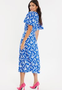 Flödande blå klänning med vitt blommönster, korta volangärmar, åtsittande midja och kjol i medellängd. Bärs med rosa högklackade skor.