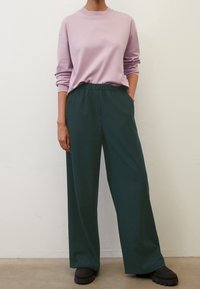 Lilac pullover with long sleeves paired with dark green wide-leg pants. Pants feature an elastic waistband; footwear has thick soles.