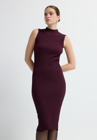 Prążkowana, bezrękawnikowa sukienka o dopasowanym kroju w głębokim burgundzie. Posiada wysoki dekolt i obcisły fason, sięgającym do połowy łydki z subtelnym wykończeniem.