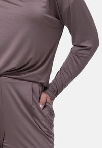 Långärmad tröja i dämpad mauve-nyans, med avslappnad passform, mjuk textur och sidofickor. Slät design med subtil lyster.