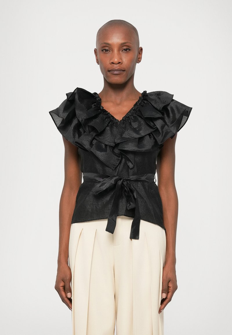 Mustmustadega must tops ja V-kaelusega ning lipsuga vöökoht, millel on tekstuuriga kangas ja kihilised varrukad. Kombineeritud kõrge vöökohtadega kreemjate pükstega.