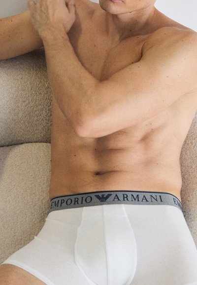 Fehér pamut boxer alsónadrág szürke derékrésszel, amelyen az "Emporio Armani" logó található. Az anyag simának és testhezállónak tűnik.