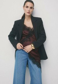 Czarna marynarka na bordowej koszulce na ramiączkach ozdobionej koronką, w połączeniu z szerokimi dżinsami o luźnych nogawkach. Do stroju dodano złotą bransoletkę na nadgarstku.