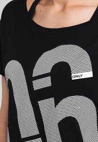 Musta T-paita, jossa on suuret valkoiset pilkulliset numerot ja pieni "ONLY PLAY" -labeli oikeassa alakulmassa. Valmistettu pehmeästä ja hengittävästä kankaasta.