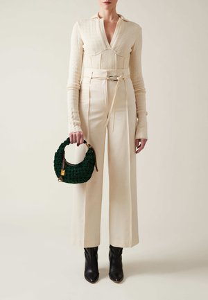 Cream textured sweater, high-waisted cream wide-leg trousers, and black pointed ankle boots. Holding a dark green woven bag with gold accents.