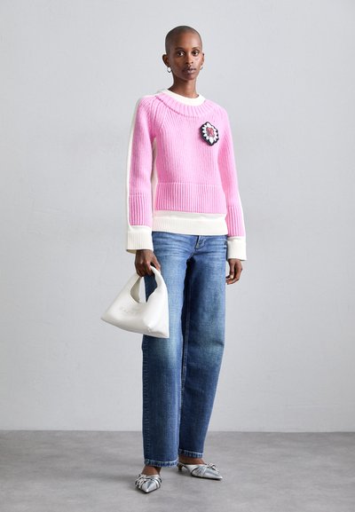 Pull en tricot rose avec des finitions blanches et un patch floral, associé à un jean droit bleu, des ballerines argentées à bout pointu et un sac à main blanc.
