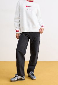 Felpa grigia con dettagli rossi, con il logo Nike. Jeans neri larghi con accessori dorati. Scarpe argentate con dettagli neri.