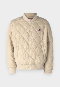 Chaqueta acolchada beige con cuello acanalado, botones a presión y un pequeño parche de logo. Presenta un patrón de diamantes y puños y dobladillo elásticos.