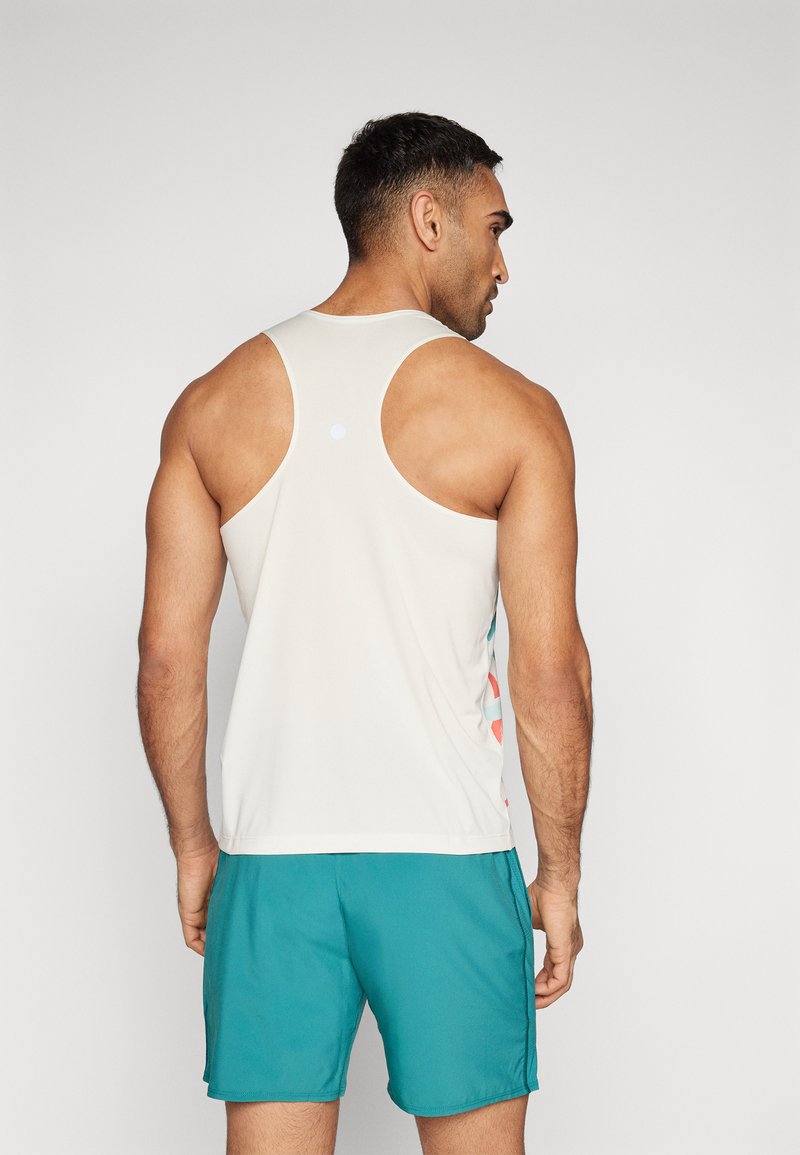 Top sin mangas de tejido ligero en color blanco roto, con diseño de espalda nadadora, detalles en colores contrastantes en los laterales, combinado con pantalones cortos color azul verdoso.