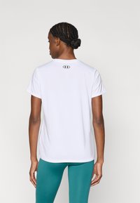 Balti sportinė marškinėliai su apvalia apykakle ir trumpomis rankovėmis, ant viršutinės nugaros dalies yra mažas juodas logotipas. Lygus tekstūros, prigludęs dizainas.