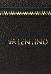 Piele neagră texturată cu un fermoar auriu vizibil și logo-ul „VALENTINO” embosat în litere aurii pe față.