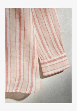 Manche longue rayée rose pâle et blanche avec poignets, suspendue sur un fond neutre.