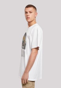 Camiseta de algodón blanca con un diseño gráfico de un personaje en una cápsula, con mangas cortas y un corte relajado.