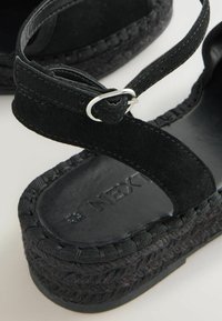Zwarte suède espadrille sandaal met een geweven jute zool. Voorzien van een enkelbandje dat met een zilveren gesp is bevestigd; soepel zwart voetbed met logo.