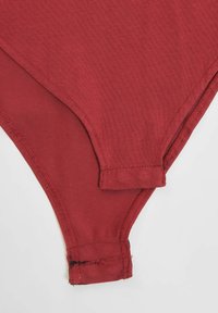 Rød stoff bikini-bunn med strukturert overflate. Har en lav midje og sømte kanter, inkludert en liten overlapning øverst.