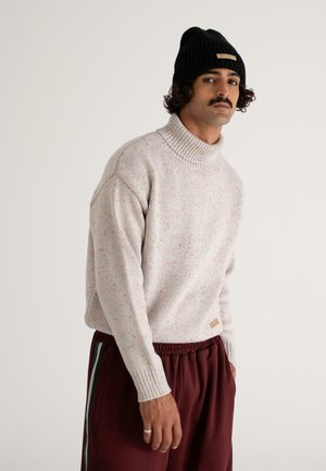 Light grey, textured knit sweater with a high collar, featuring speckles of color. Paired with burgundy elastic waistband pants.