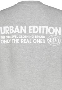 Grauer Sweatshirt mit großem weißen Text auf dem Rücken: "URBAN EDITION DIE SUBLEVEL MODEMARKE NUR DIE ECHTEN EST. 1991 SBLVI KOLLEKTION."