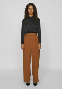 Black long-sleeve blouse with gathered neckline paired with high-waisted, wide-leg brown trousers; black pointy-toed shoes; smooth textures.
