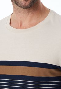 Beige Baumwoll-T-Shirt mit Rundhalsausschnitt und horizontalen Streifen in Marineblau, Braun und Weiß. Sanfte Textur mit lockerer Passform.