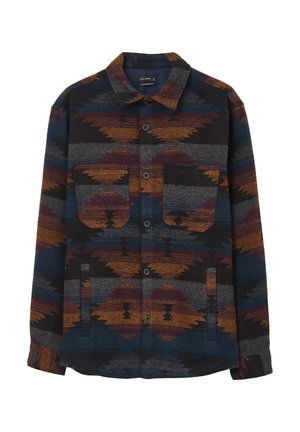 Veste chemise en tissu avec un motif géométrique dans des tons de bleu, orange et gris. Dotée d'un devant à boutons et de deux poches poitrine.